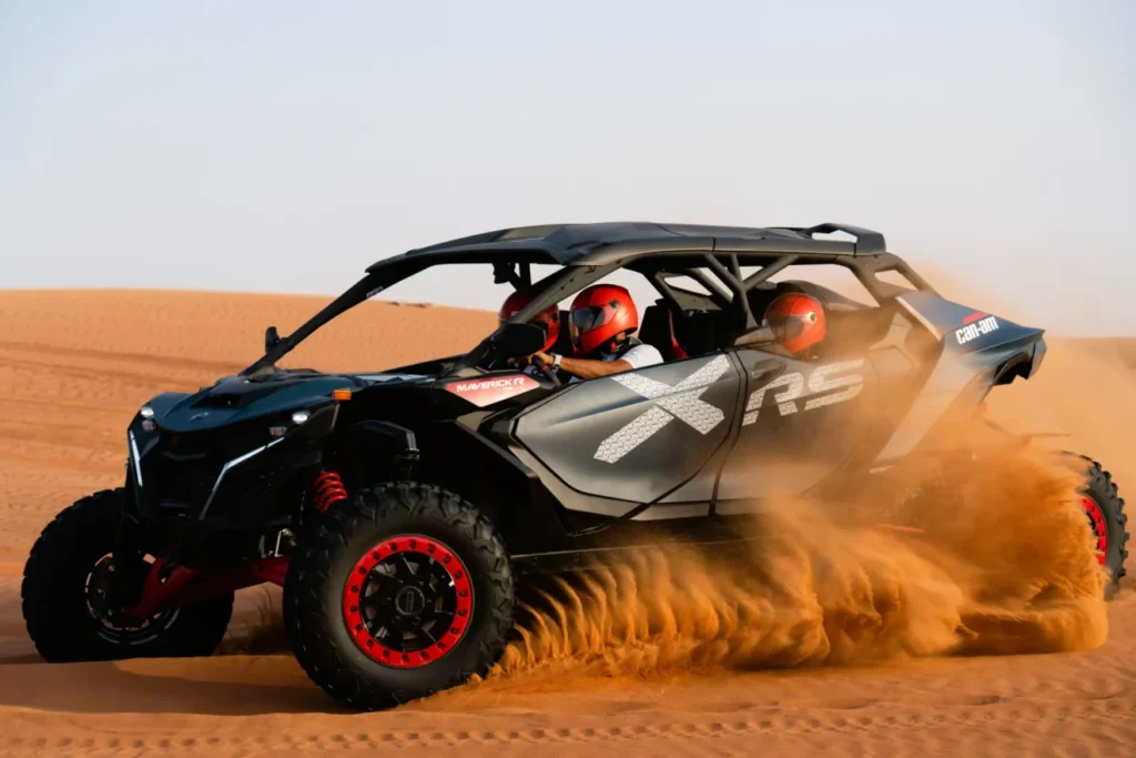 Can-Am Maverick XRS 4-seater dune buggy kicking up sand while racing across desert dunes with helmeted riders