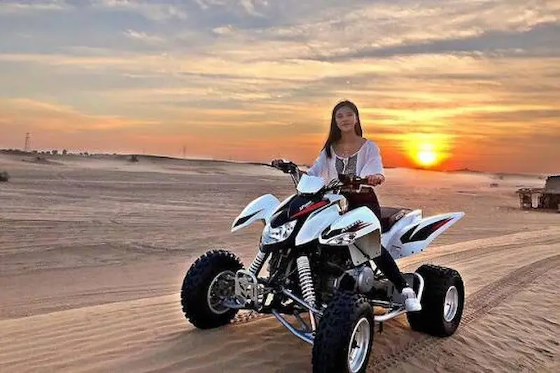 Tourist riding a quad bike across golden sand dunes in Dubai desert
