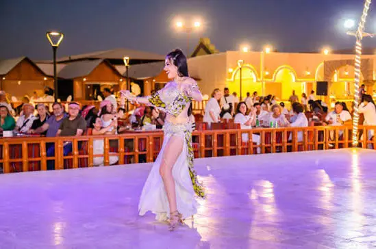 Belly dancer performing in a colorful costume at a Dubai desert safari camp at night