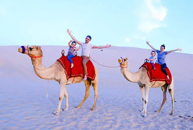 Tourist riding a camel across sand dunes during a Dubai desert safari at sunset