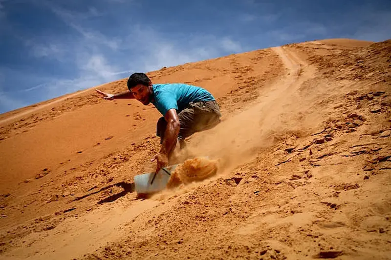 Tourist enjoying sandboarding down golden dunes in the Dubai desert