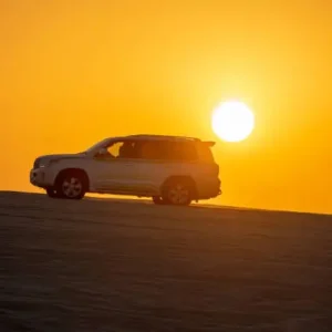 "White 4x4 SUV silhouetted against a golden sunset on sand dunes during a Dubai desert safari