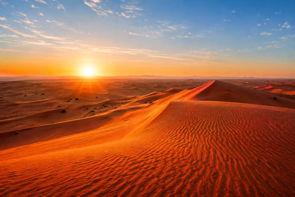 Panoramic view of the red sand dunes in Lahbab Desert Dubai illuminated by the golden sunrise under a clear blue sky.